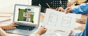 Architects and contractors review printed floor plans and a site plan on a laptop at a project coordination meeting.