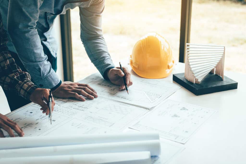 Architects reviewing construction plans and contracts at a desk with safety helmet and architectural.