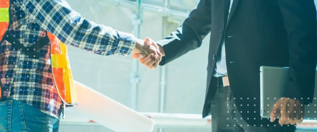 Two professionals shake hands at a construction site, symbolizing agreement and partnership.