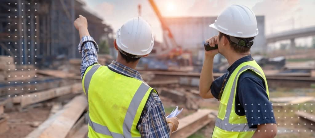 Two construction workers in safety vests and helmets inspecting a construction site.