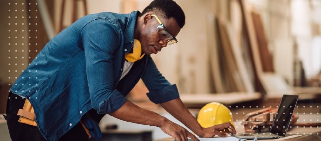 Construction worker analyzing blueprints and plans at a woodworking shop.