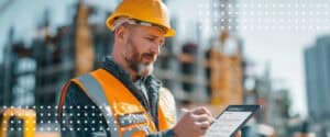 A worker in a hard hat checks a tablet on site, where the construction contract terms of a project get applied.